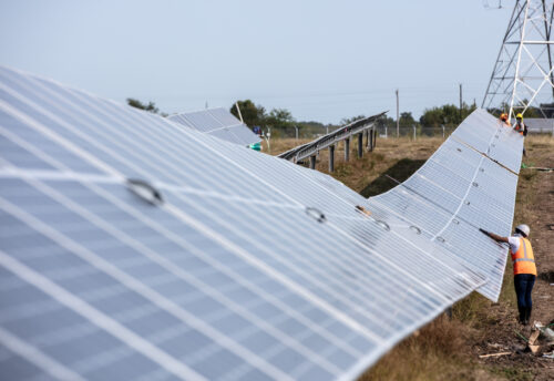 A person in an orange vest working on a long row of solar panels.