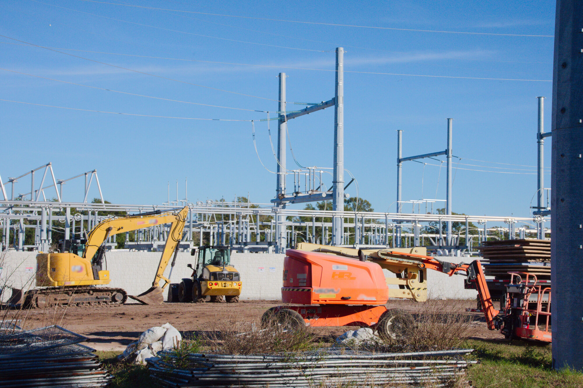 An image of a construction site with heavy machinery and an electrical substation under a clear blue sky